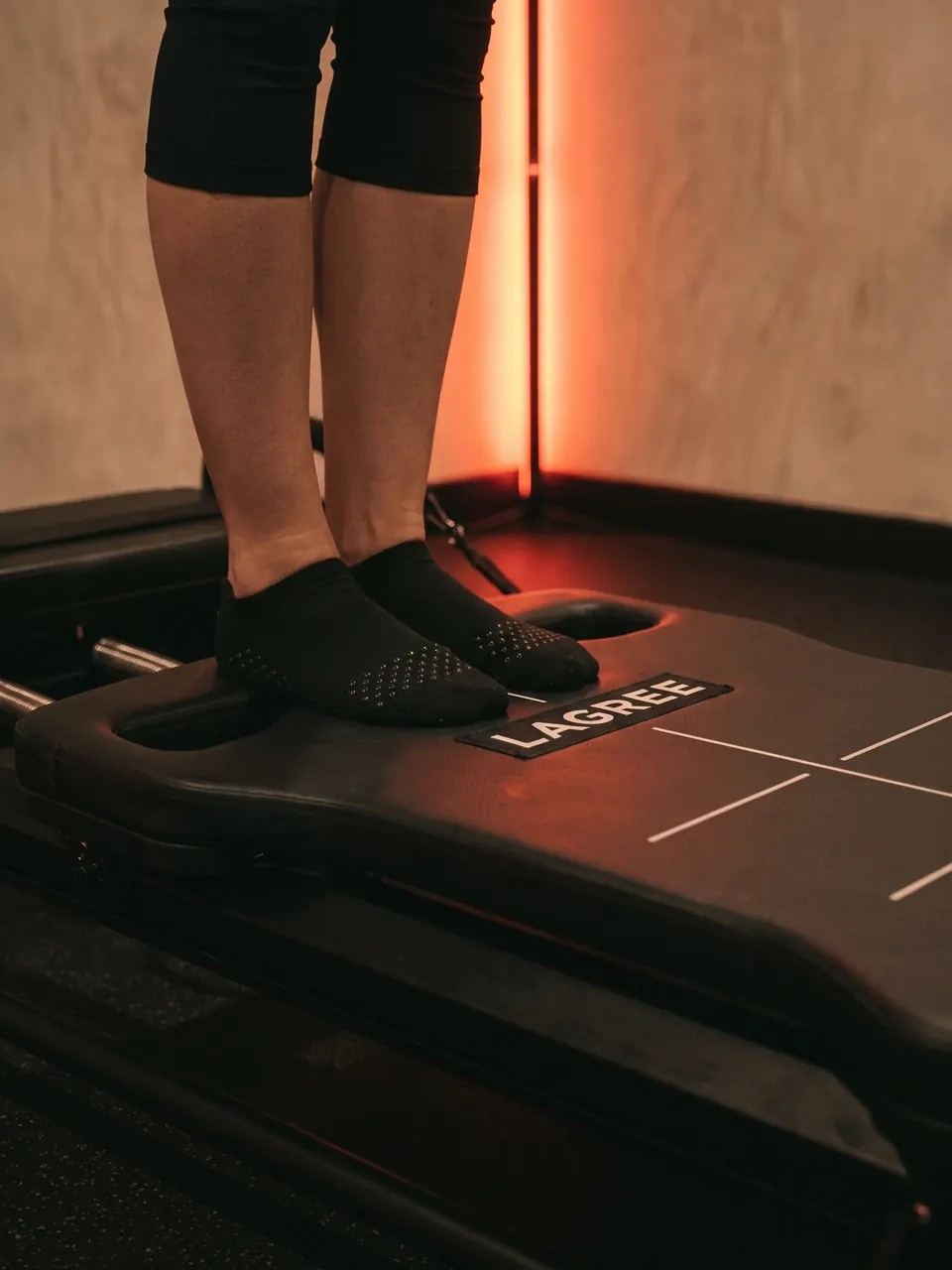 Deux pieds en chaussettes antidérapantes sur le chariot d’une Micro Pro, à côté de l’étiquette LAGREE